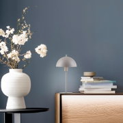 Minimalistische Tischleuchte in Weiß mit halbrundem Schirm auf Holz-Sideboard neben Bücherstapel und Keramikvase mit weißen Blüten, Frontansicht auf Augenhöhe