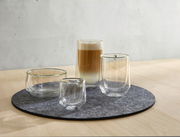 Vier doppelwandige Gläser auf einem runden Filzuntersetzer, perspektivisch von vorne rechts fotografiert, mit einem Latte Macchiato im größten Glas.