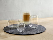 Vier doppelwandige Gläser auf einem runden Filzuntersetzer, perspektivisch von vorne rechts fotografiert, mit einem Latte Macchiato im größten Glas.
