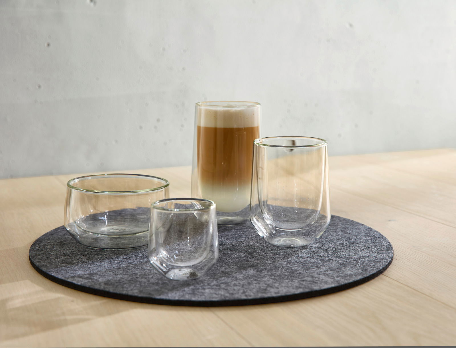 Vier doppelwandige Gläser auf einem runden Filzuntersetzer, perspektivisch von vorne rechts fotografiert, mit einem Latte Macchiato im größten Glas.