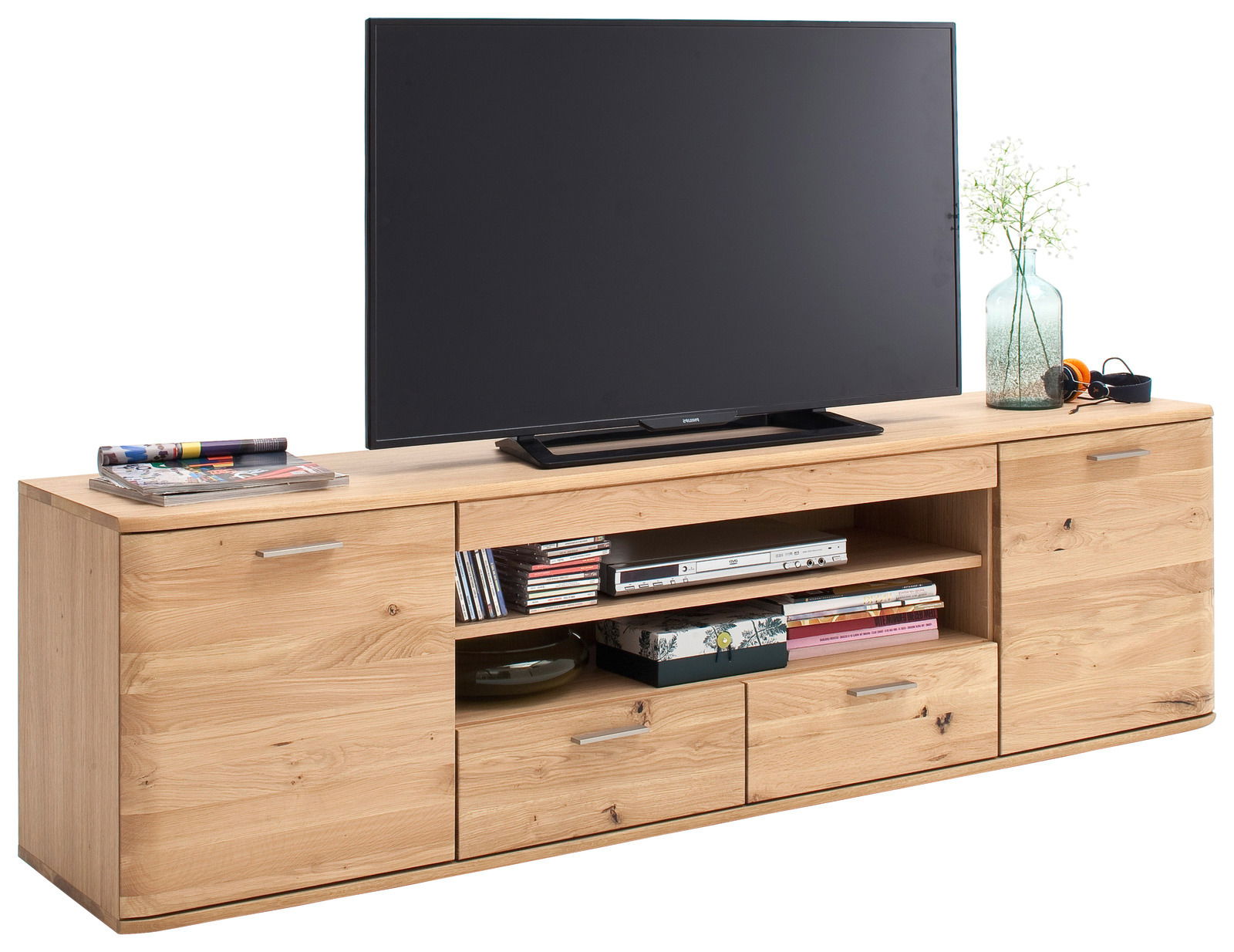 XL-TV-Lowboard aus Holz mit zwei Schubladen und offenen Regalfächern, darauf ein großer Fernseher, Zeitschriften und Dekoration. Frontalansicht.