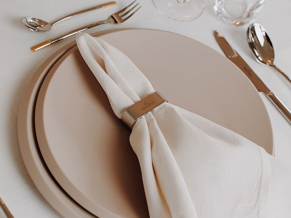 Stilvoll eingedeckter Tisch, mit hellen Tellern, Serviette und glänzendem Besteck für ein scheinendes Abendessen