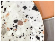 Detailaufnahme aus leicht schräger Draufsicht: runder Terrazzo-Deckel in Weiß mit schwarzen, grauen und roséfarbenen Sprenkeln auf einem Behälter in Terrakotta und Grau