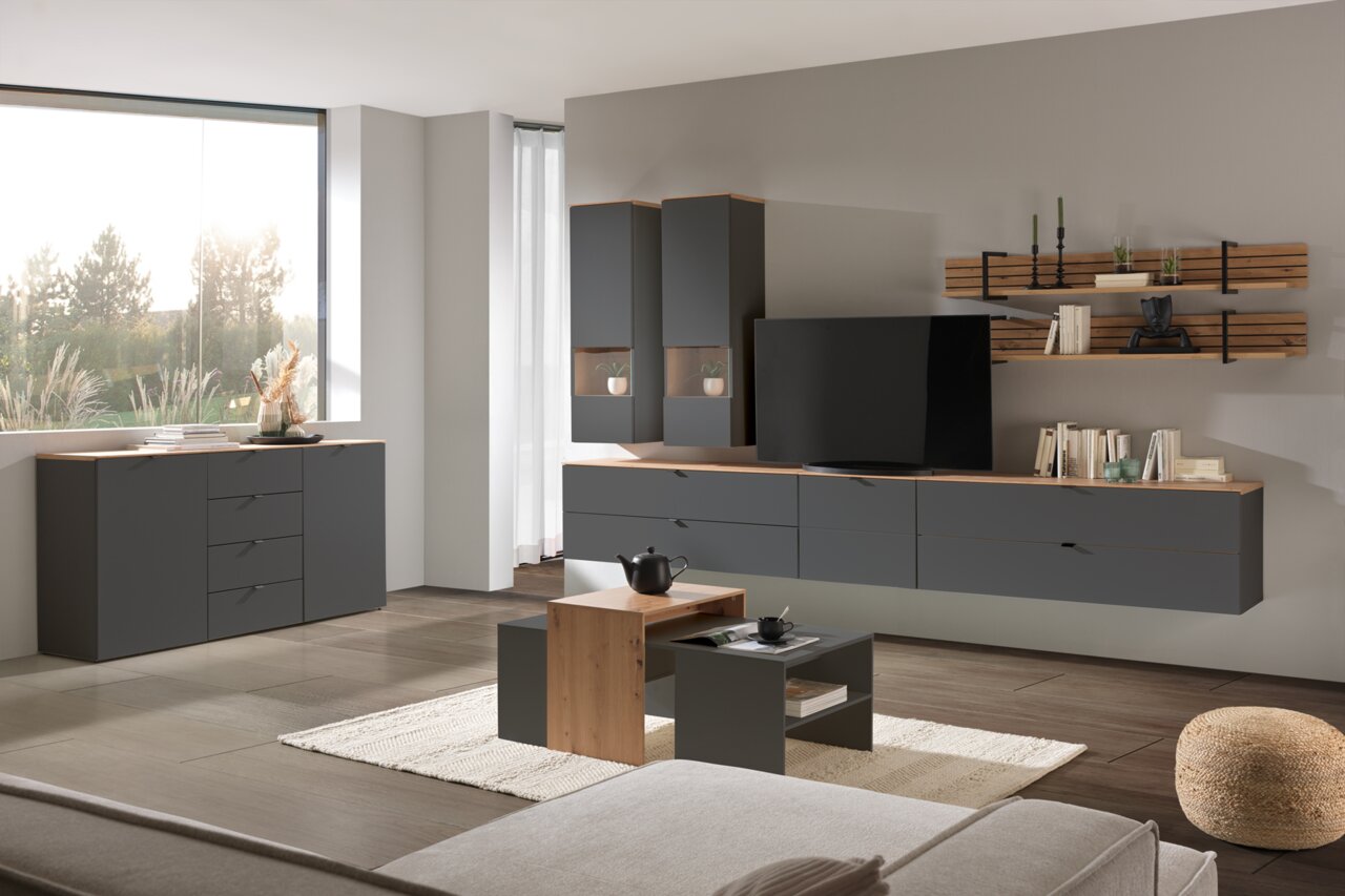 Moderne Wohnzimmermöbel in dunklem Grau mit Holzakzenten, bestehend aus Hängeschränken, TV-Lowboard, Wandregal und Couchtisch, aus seitlicher Perspektive fotografiert.