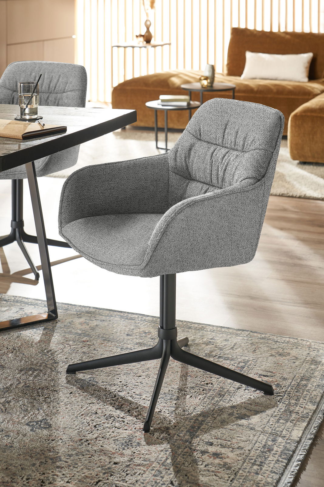 Grauer Armlehnstuhl mit schwarzem Metallgestell, seitliche Perspektive, in modernem Wohnambiente.