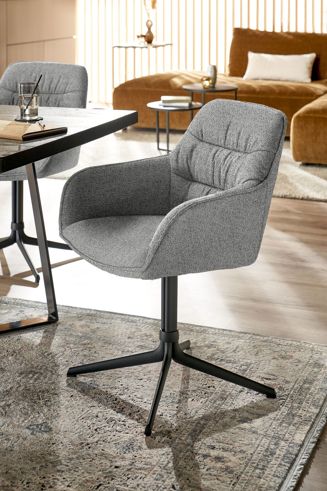 Grauer Armlehnstuhl mit schwarzem Metallgestell, seitliche Perspektive, in modernem Wohnambiente.