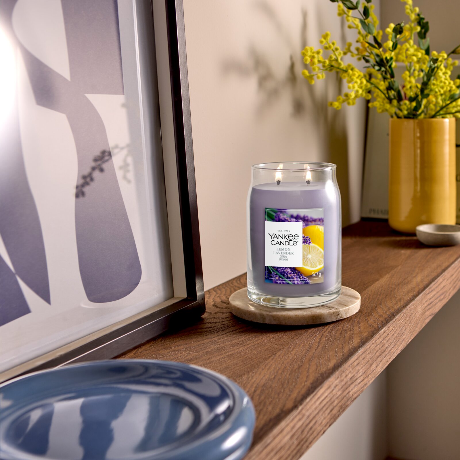Frontalansicht einer brennenden Yankee Candle Lemon Lavender Duftkerze mit zwei Dochten im Glas, dekorativ auf einem Holzregal arrangiert