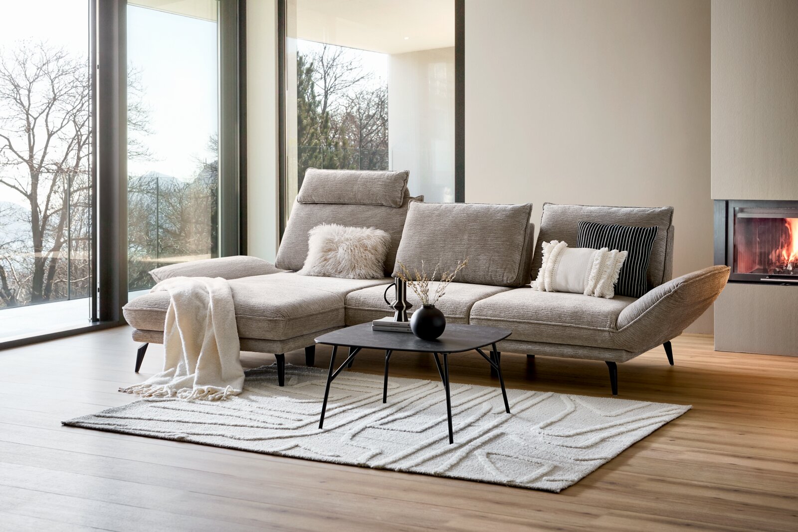 Modernes Longchair-Sofa in einem hellen Wohnzimmer mit großen Fenstern, Blick auf die linke Seite des Sofas.