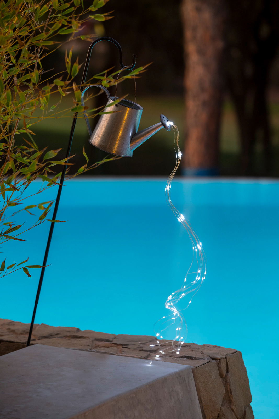 Solarleuchte in Form einer Gießkanne, die an einem Haken hängt und Lichterketten wie Wasserstrahlen ausgießt, seitliche Perspektive