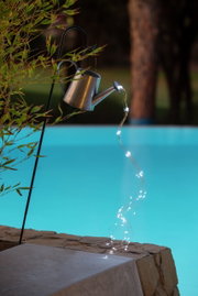 Solarleuchte in Form einer Gießkanne, die an einem Haken hängt und Lichterketten wie Wasserstrahlen ausgießt, seitliche Perspektive