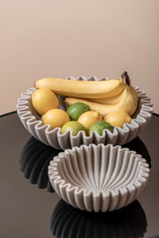 Zwei graue Schalen mit gewelltem Rand, gefüllt mit Bananen, Zitronen und Limetten, auf einem schwarzen Tisch aus der Vogelperspektive.