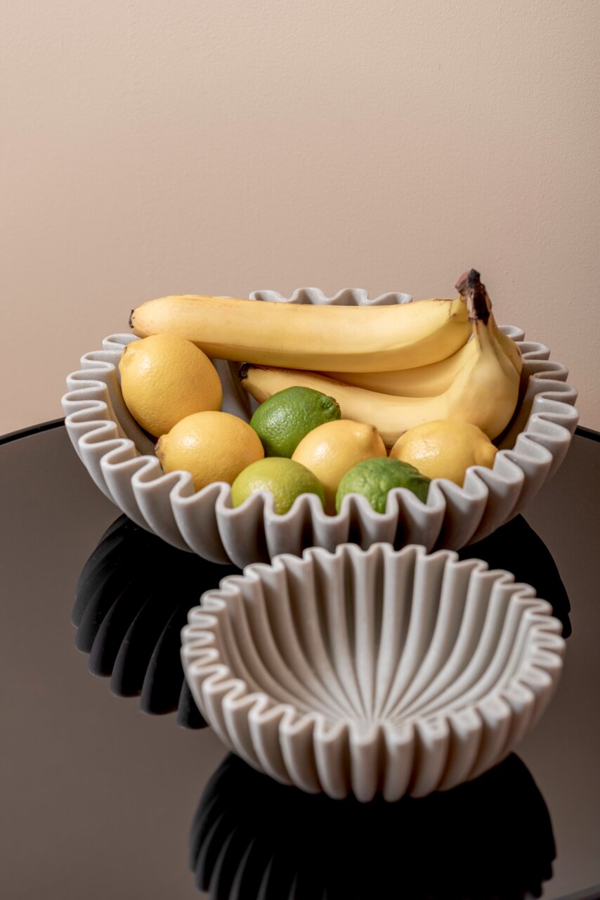 present time Schale Large WAVE Zwei graue Schalen mit gewelltem Rand, gefüllt mit Bananen, Zitronen und Limetten, auf einem schwarzen Tisch aus der Vogelperspektive.