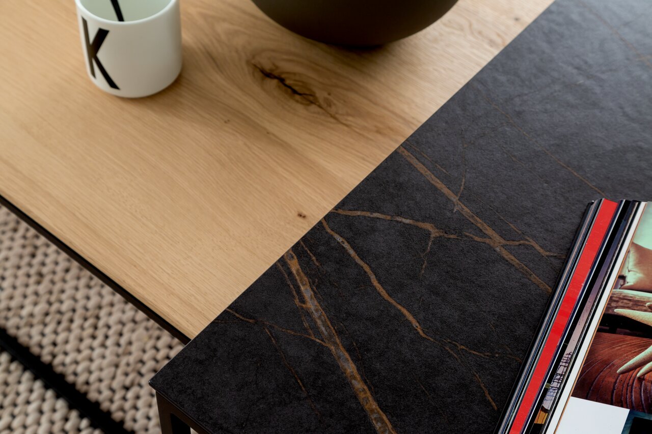 Nahaufnahme eines modernen Beistelltisches mit einer Kombination aus heller Holz- und dunkler Steinoptik, von oben fotografiert.