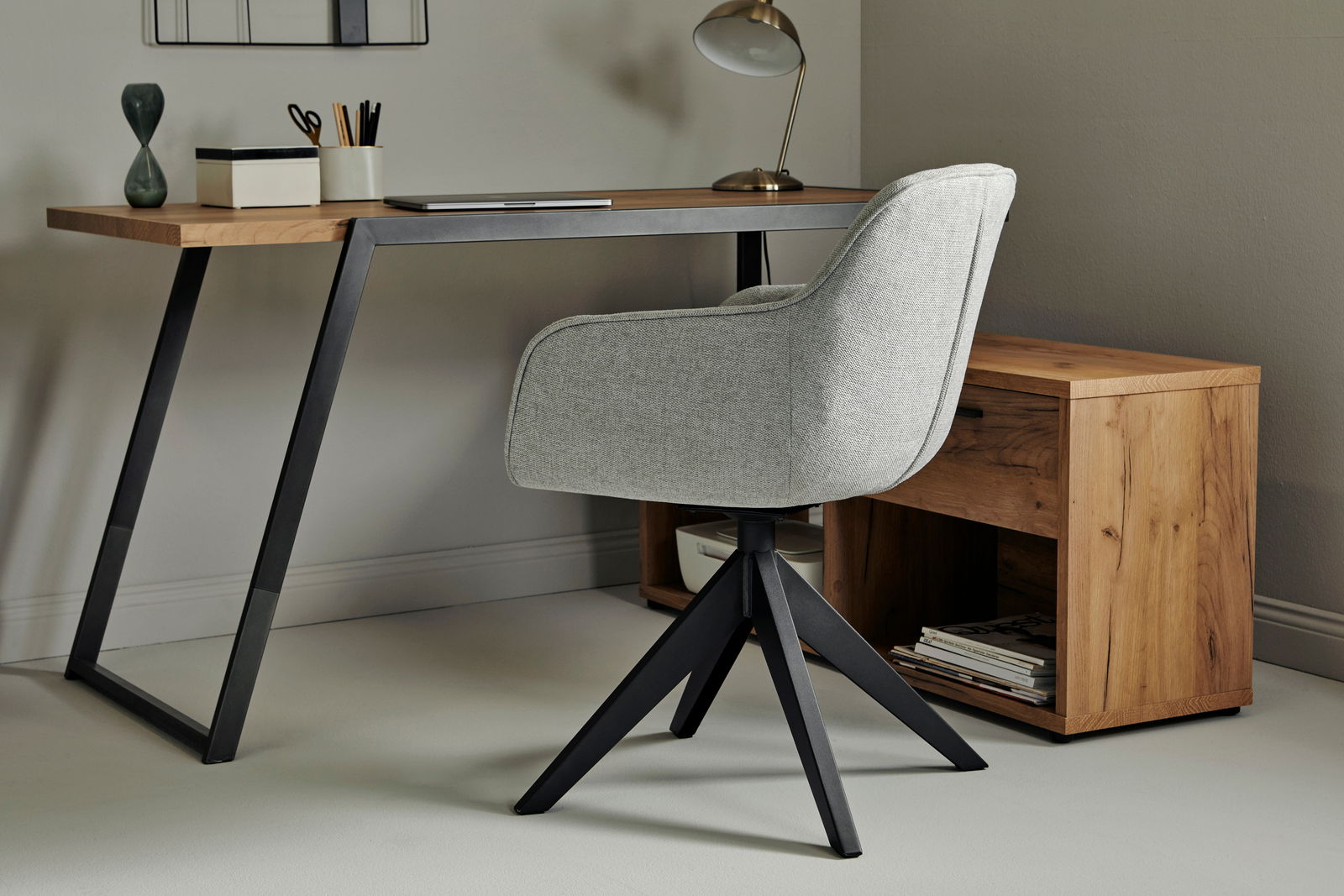 Moderner grauer Drehstuhl mit schwarzem Metallgestell, seitliche Perspektive, neben einem Schreibtisch aus Holz.