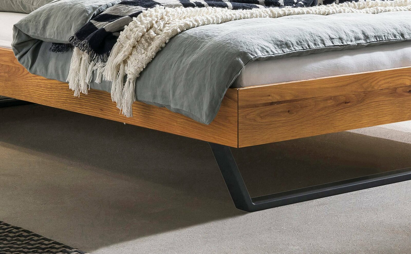 Nahaufnahme eines modernen Bettgestells aus Holz mit Metallbeinen, seitliche Perspektive.