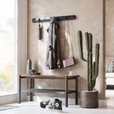 Moderne Wandgarderobe mit Haken, an der ein Mantel, eine Tasche und eine Flasche hängen, daneben ein Kaktus in einem Topf, im Vordergrund eine Bank mit Kopfhörern und einer Trinkflasche, Perspektive von der Seite