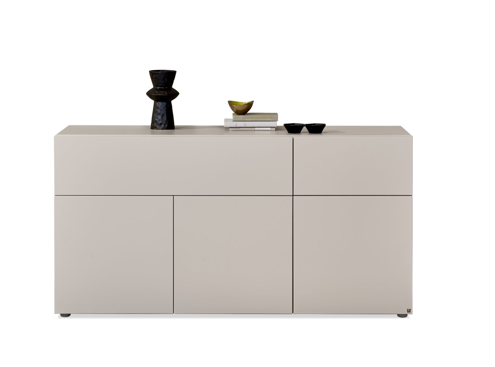 Modernes, griffloses Sideboard in hellem Greige mit geometrisch aufgeteilten Fronten und dekorativen Accessoires, frontal aus leichter Obersicht dargestellt.