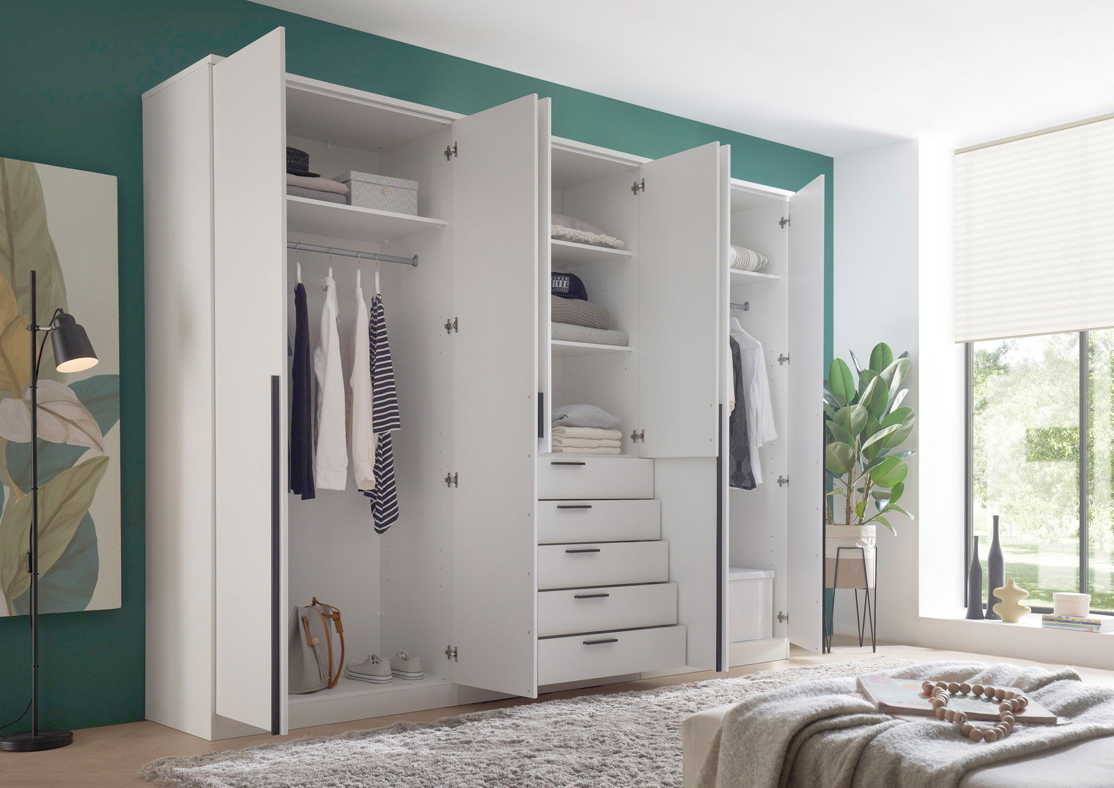 Moderner, weißer Drehtürenschrank mit sechs Türen, teilweise geöffnet, zeigt Innenfächer, Kleiderstangen und Schubladen. Perspektive von vorne links.