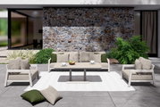 Moderne loungeset met een driezitsbank en twee fauteuils in een elegante buitenruimte, gezien vanaf de voorkant. De set is versierd met beige kussens en groene accenten, en staat op een wit tapijt voor een stenen muur.