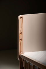 Detailansicht eines Anstellbetts mit Holzverzierungen und weißer Matratze.