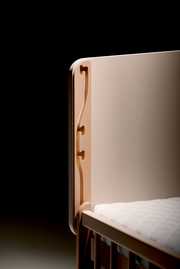 Detailansicht eines Anstellbetts mit Holzverzierungen und weißer Matratze.