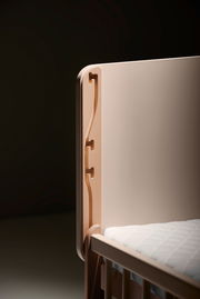 Detailansicht eines Anstellbetts mit Holzverzierungen und weißer Matratze.