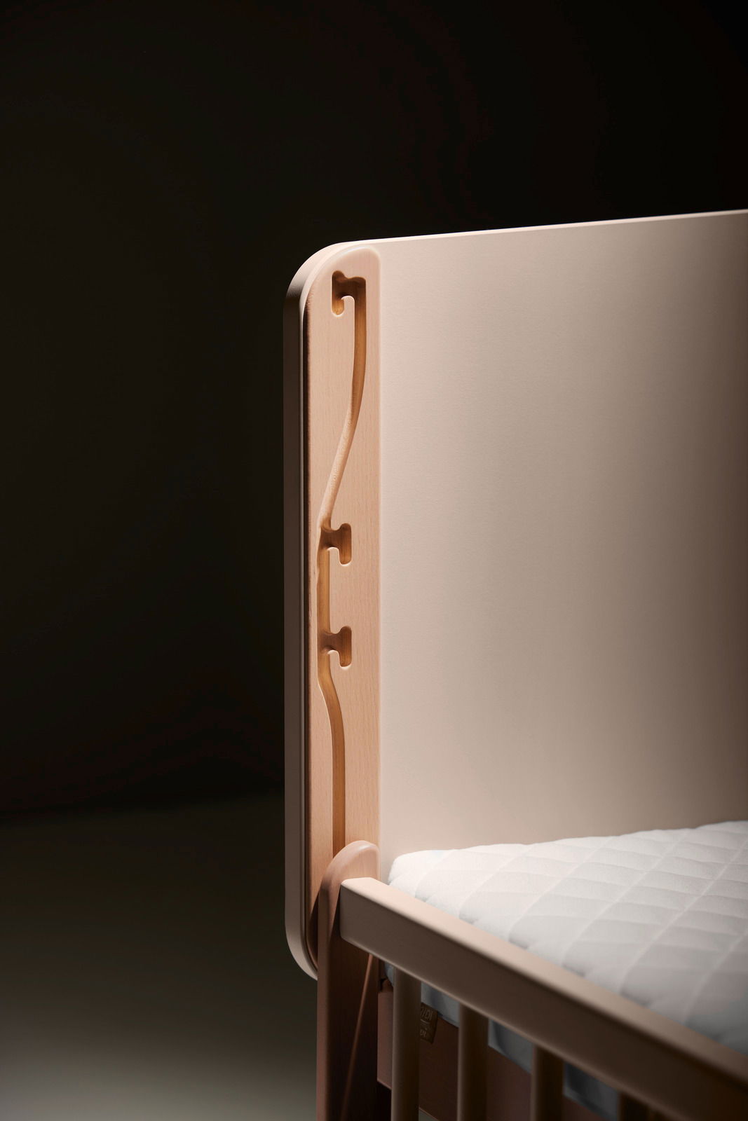 Detailansicht eines Anstellbetts mit Holzverzierungen und weißer Matratze.