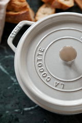 Obere Perspektive auf einen runden, grauen Bräter Cocotte mit Deckel und Griffen, umgeben von Brotstücken.