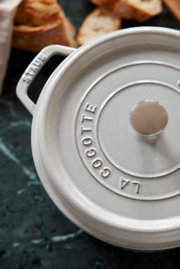Obere Perspektive auf einen runden, grauen Bräter Cocotte mit Deckel und Griffen, umgeben von Brotstücken.