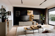 Moderne Wohnzimmer-Wandkombination Venjakob VANYA in einem stilvollen Raum mit schwarzer Akzentwand, TV, Pflanzen und dekorativen Elementen, seitliche Perspektive.