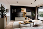 Moderne Wohnzimmer-Wandkombination Venjakob VANYA in einem stilvollen Raum mit schwarzer Akzentwand, TV, Pflanzen und dekorativen Elementen, seitliche Perspektive.