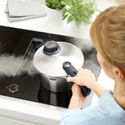 Draufsicht auf einen dampfenden Schnellkochtopf auf einem Herd, gehalten von einer Person.