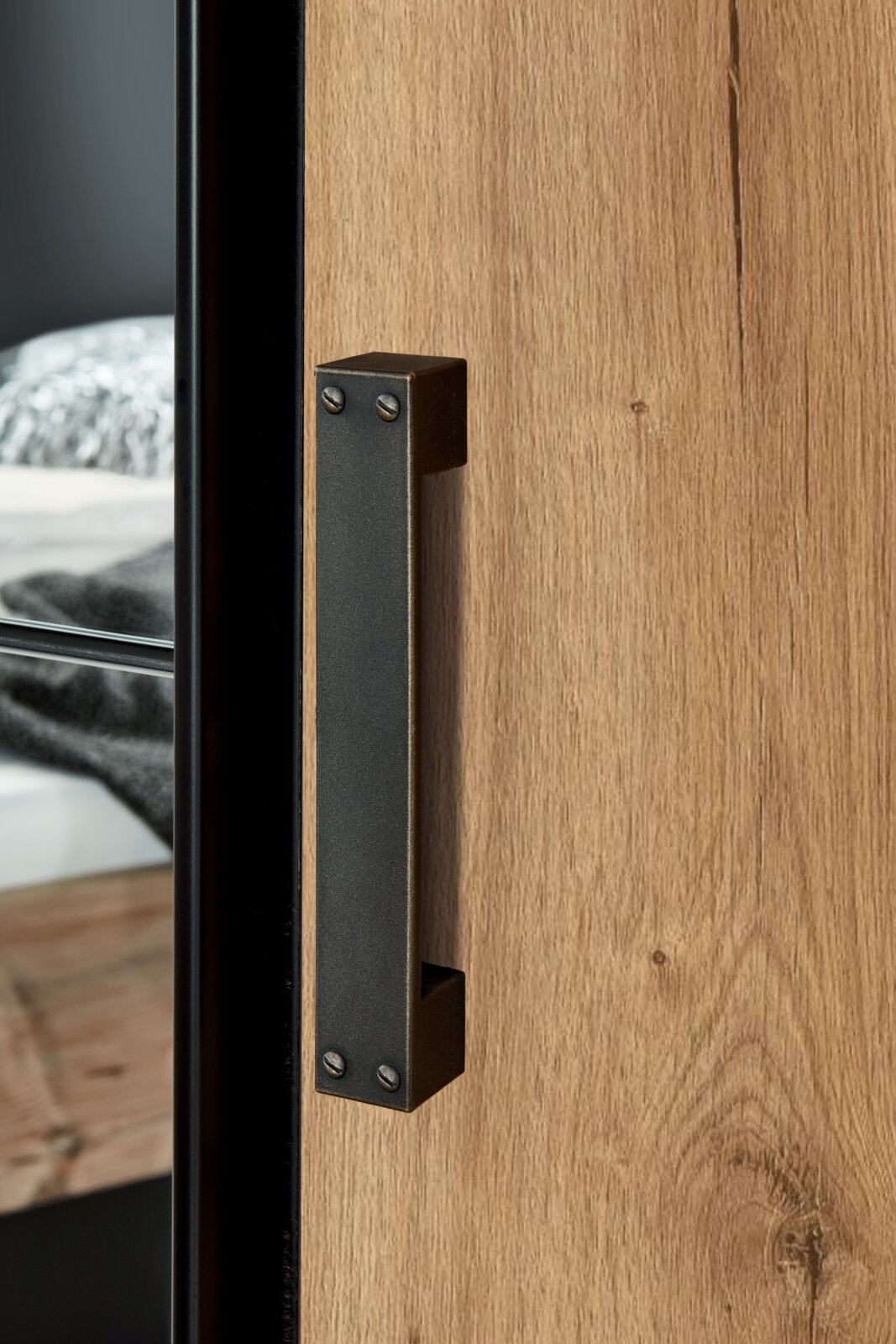 Nahaufnahme eines Türgriffs an einem Drehtürenschrank aus Holz mit Metallakzenten, seitliche Perspektive.