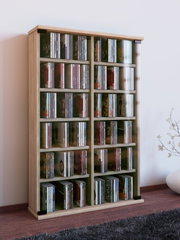 Hohes CD-/DVD-Regal in heller Holzoptik mit mehreren Fächern, gefüllt mit CDs, in Wohnraumumgebung; Perspektive: leicht schräg von vorne links auf Augenhöhe