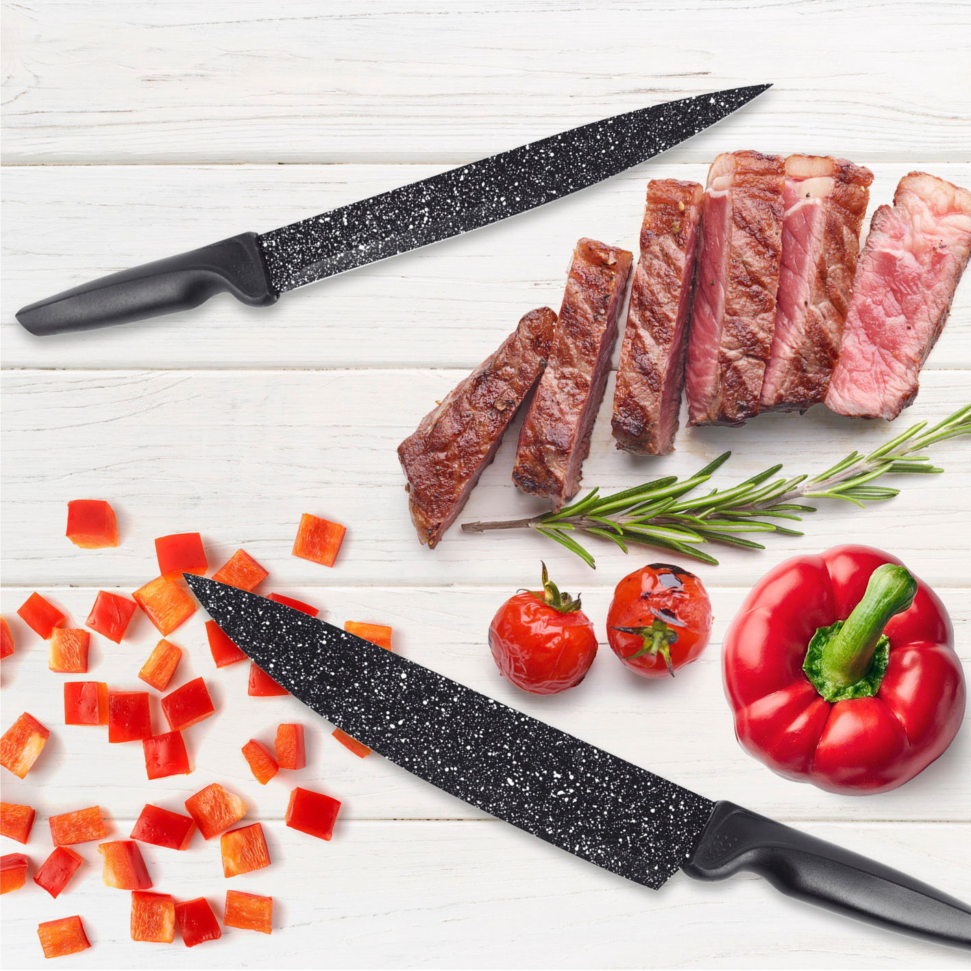 Zwei schwarze Messer mit gesprenkelter Klinge auf einem weißen Holztisch, umgeben von geschnittenem Steak, Paprikawürfeln, Tomaten und einem Rosmarinzweig. Draufsicht.