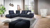 Moderner Wohnraum mit einem eleganten, weißen Sessel in der rechten Ecke, umgeben von einem großen, dunkelblauen Sofa in L-Form. Die Perspektive zeigt den Raum von vorne mit Blick auf große Fenster, die viel Tageslicht hereinlassen.