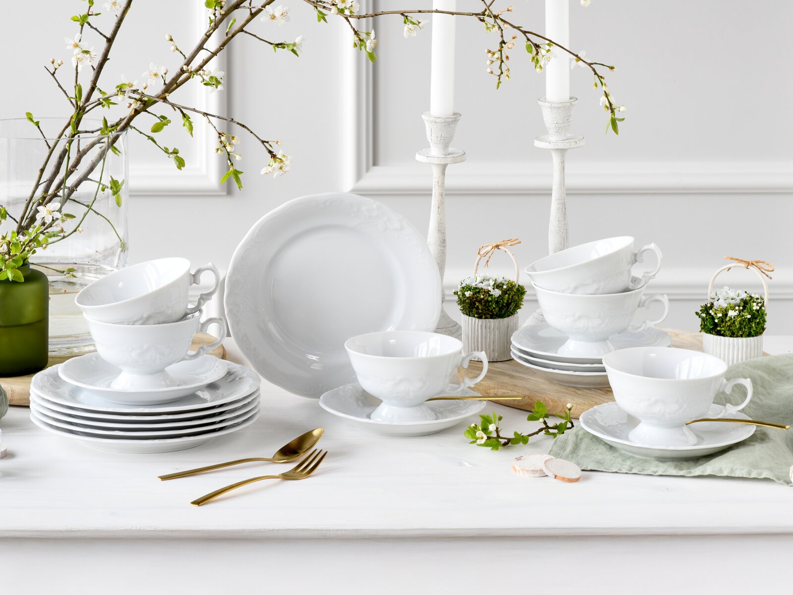Creatable Kaffeeservice 18-tlg FREDERIKE Weißes Porzellan-Geschirrset mit Tassen, Untertassen und Tellern im klassischen Reliefdesign, dekoriert mit Frühlingszweigen und Kerzenleuchtern, fotografiert in frontaler Tischansicht leicht von oben.