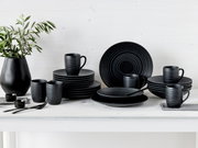 Schwarzes Kombiservice 24-tlg auf einem weißen Tisch, bestehend aus Tellern, Tassen und Schalen, mit einer modernen, matten Oberfläche. Perspektive: Frontalansicht.