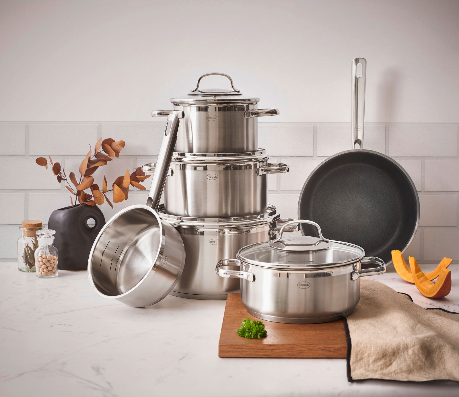 Topfset ELEGANCE 6-tlg. aus Edelstahl, bestehend aus mehreren Töpfen und einer Pfanne, auf einer Küchenarbeitsplatte arrangiert. Perspektive von vorne.