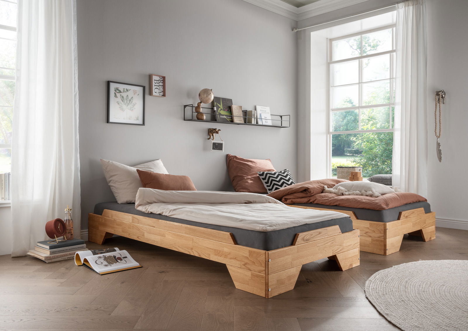 Zwei moderne Stapelbetten aus Holz in einem hellen Raum mit großen Fenstern, seitliche Perspektive.