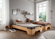 Zwei moderne Stapelbetten aus Holz in einem hellen Raum mit großen Fenstern, seitliche Perspektive.