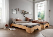 Zwei moderne Stapelbetten aus Holz in einem hellen Raum mit großen Fenstern, seitliche Perspektive.