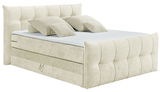 Beiges Boxspringbett mit gepolstertem Kopfteil und mehreren Kissen, seitliche Perspektive