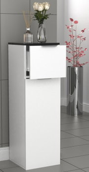 Schmaler weißer Badschrank mit schwarzer Deckplatte und zwei Fronten, obere Klappe leicht geöffnet; darauf Glasvase mit weißen Rosen und Duftstäbchen, rechts daneben hoher silberner Pflanzkübel mit rosa Zweigen, aufgenommen in leichter Seitenansicht von v
