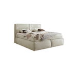Boxspringbett in seitlicher Perspektive mit beiger Polsterung, dekoriert mit Kissen und Decken.