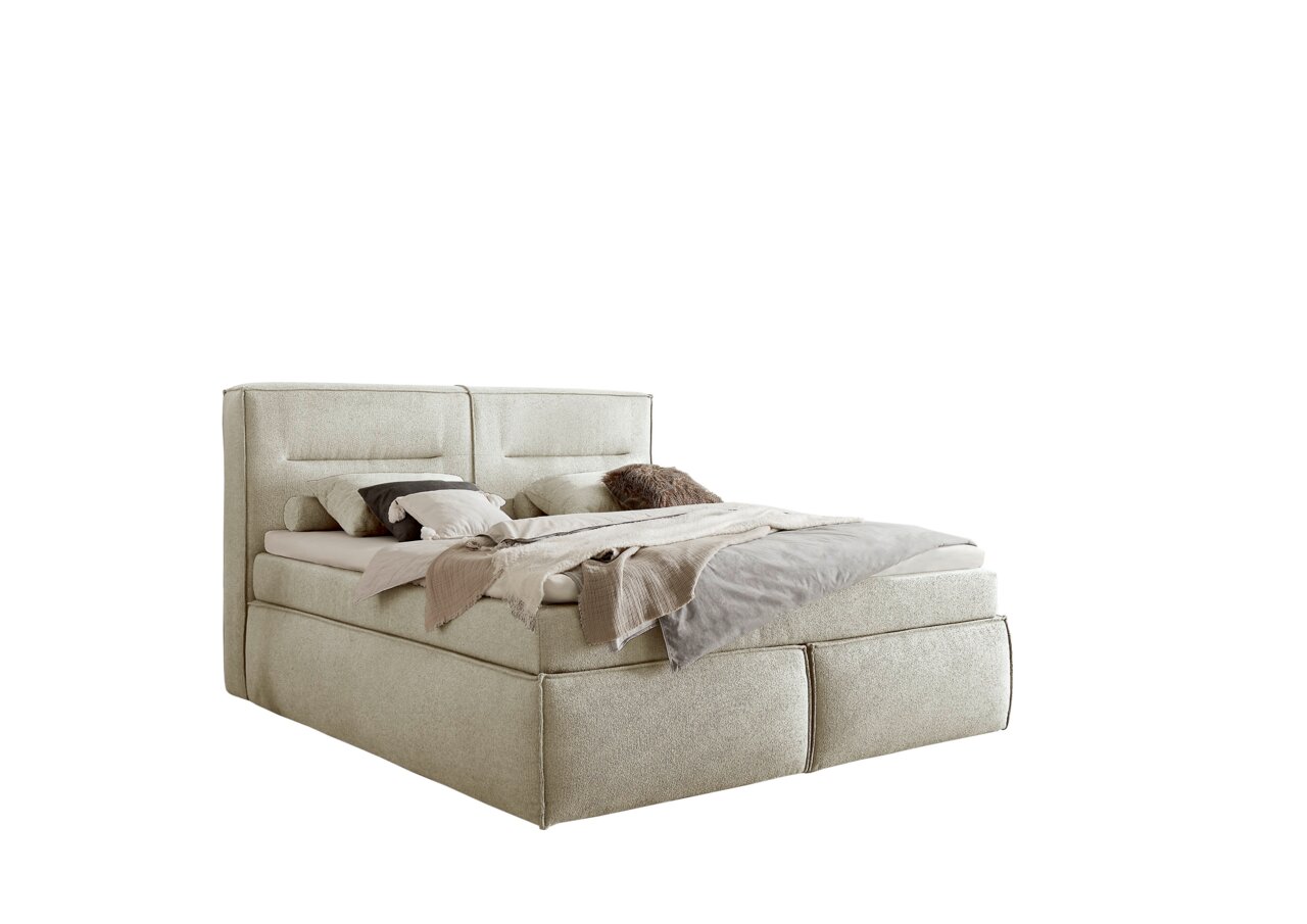 Boxspringbett in seitlicher Perspektive mit beiger Polsterung, dekoriert mit Kissen und Decken.