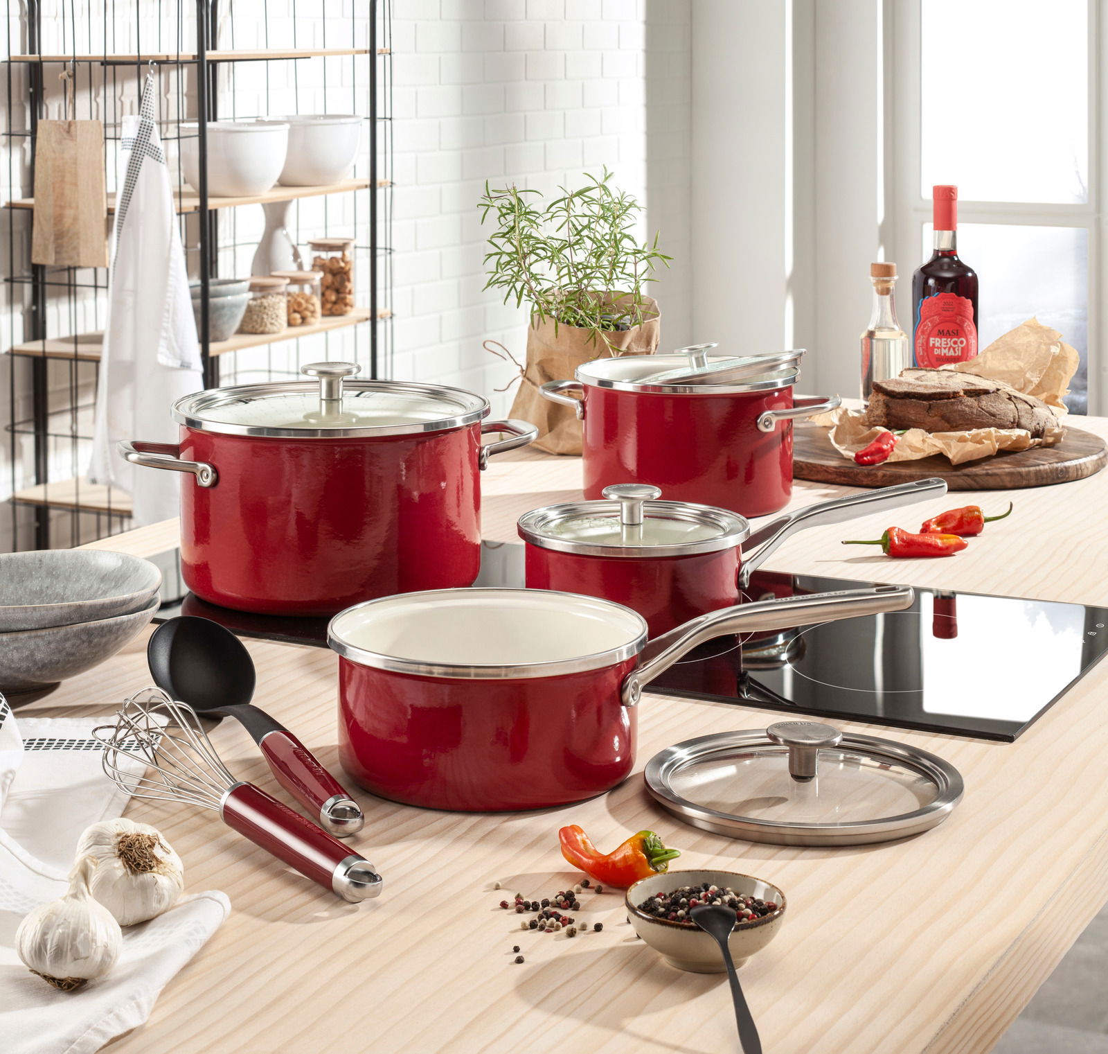 Rotes 6-teiliges Topfset aus Emaille auf einem modernen Küchentisch, fotografiert aus einer leicht erhöhten Perspektive.