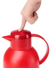 Rote Isolierkanne SAMBA 1,5L mit einem Finger, der den Deckel von oben drückt.