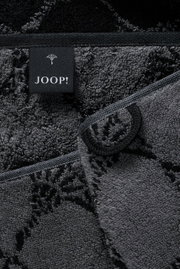 Close-up van een grijze saunadoek met een zwart label van het merk JOOP! en bloemmotieven.