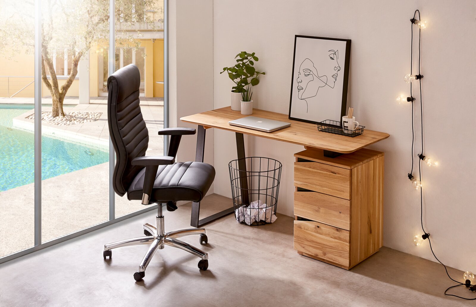 Modern houten bureau met lades, gezien vanaf de zijkant, naast een groot raam met uitzicht op het zwembad, versierd met planten en kunstwerken.